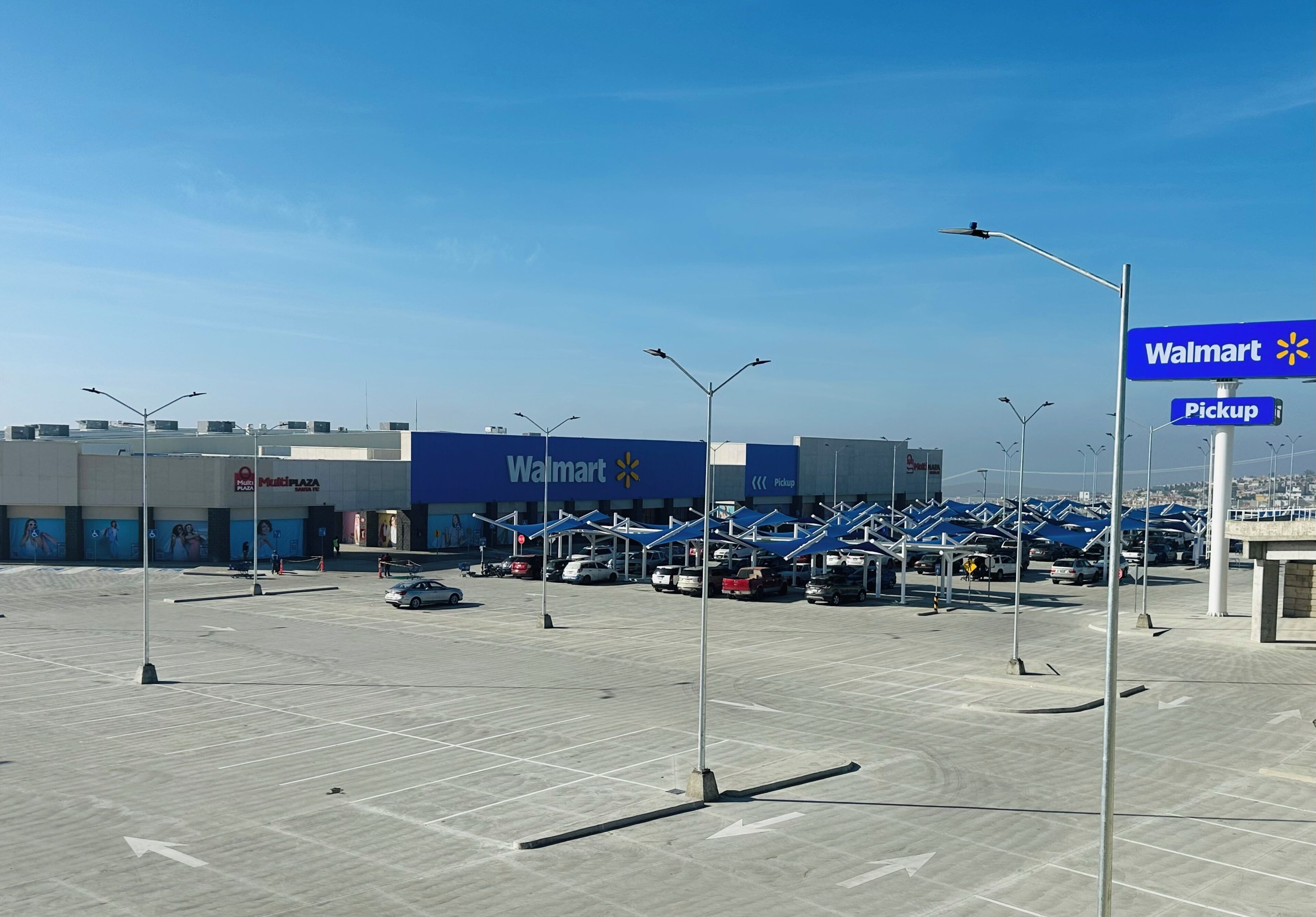Un estacionamiento con Walmart y una zona de recogida, cielo despejado y algunos coches aparcados.