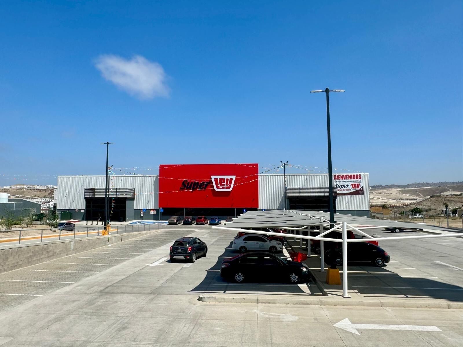 Un grand magasin Super Lowe's avec une grande enseigne rouge, un parking où sont garées plusieurs voitures et un ciel bleu dégagé.