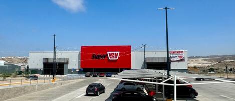 Un grand magasin Super Lowe's avec une grande enseigne rouge, un parking où sont garées plusieurs voitures et un ciel bleu dégagé.
