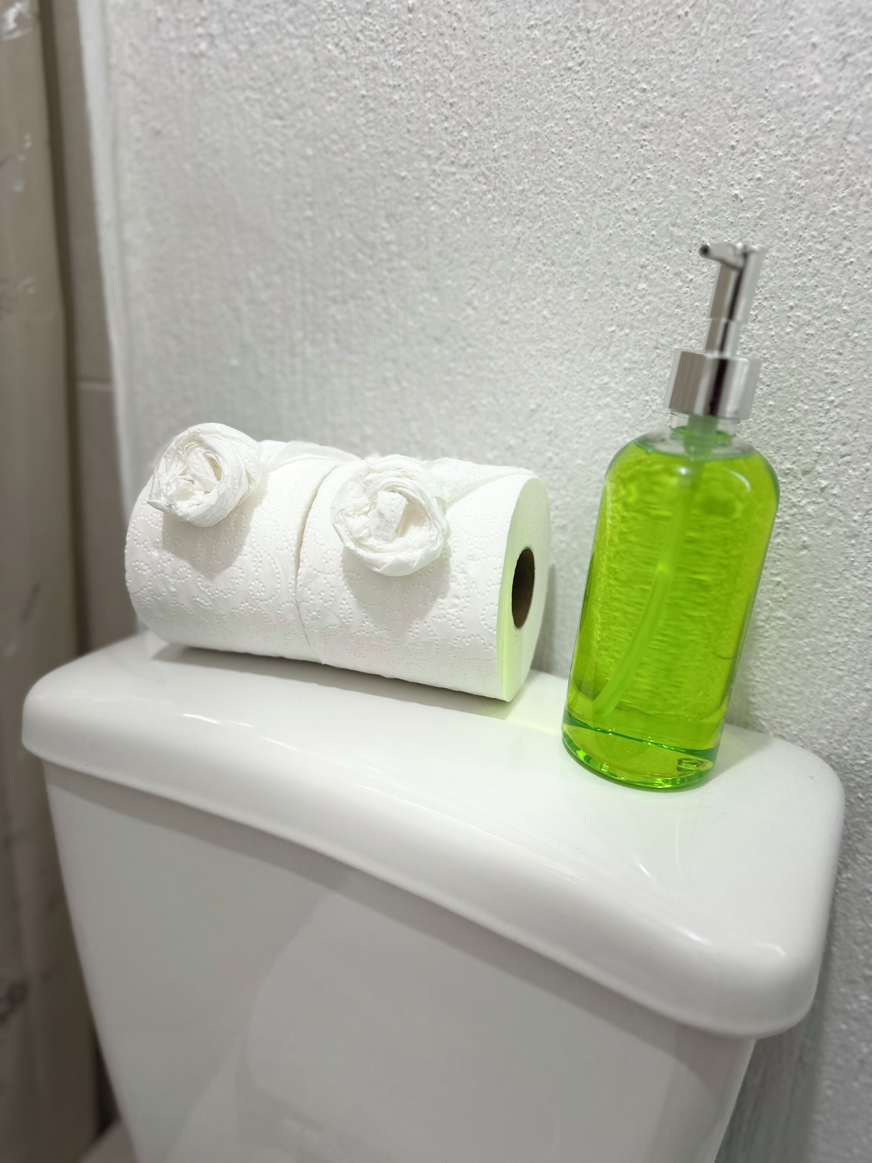 A toilet with a toilet paper roll and a green bottle on the tank.