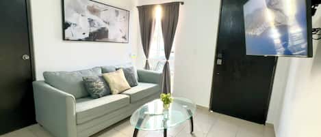 Una sala de estar con un sofá, una mesa de centro de vidrio, un televisor y un cuadro en la pared.