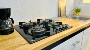Et køkken med gasblus, kaffemaskine og vask.