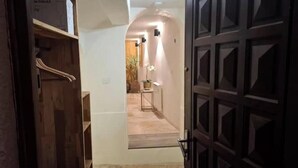 Un pasillo con una puerta de madera, una mesita con una planta y una lámpara en la pared.