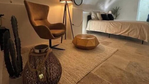 Una habitación acogedora con una cama, una silla, una lámpara y un cuenco decorativo sobre una alfombra.