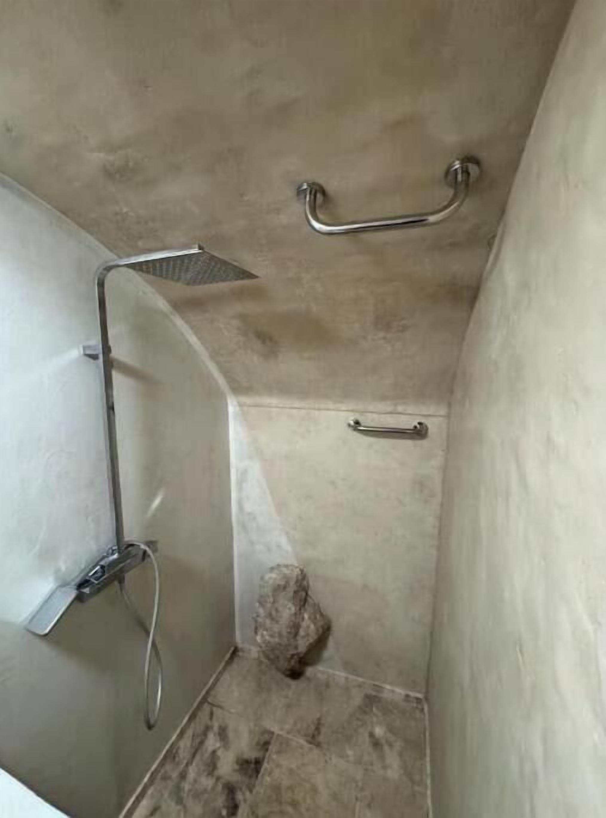 A small, enclosed shower area with a handheld showerhead, a grab bar, and a towel rack.
