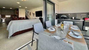 Een moderne hotelkamer met een groot bed, een zithoek met een tafel gedekt voor twee personen, een keuken met kookplaat en magnetron, en een trap naar een hoger niveau.