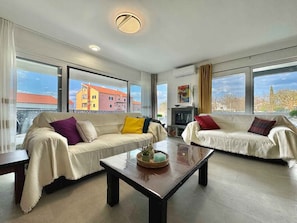 A spacious living room with two sofas, a coffee table, and large windows offering a view of colorful buildings. - Villa with swimming pool (Malinska)