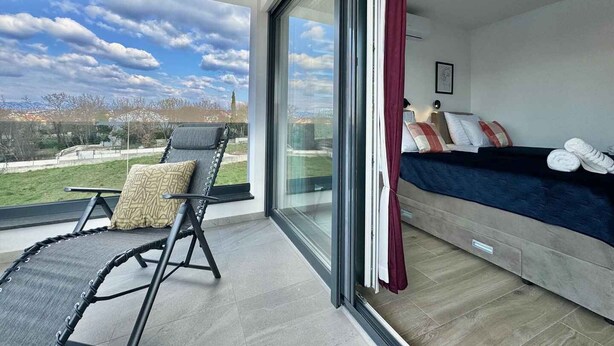 Een balkon met uitzicht, een bed met kussens en een stoel.