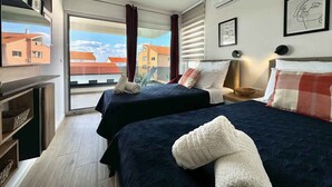 Een hotelkamer met twee bedden, een televisie, een open haard en een balkon met uitzicht over de stad.