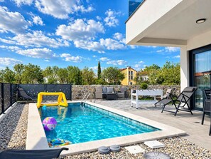 Piscina com parede de pedra, espreguiçadeiras e uma mesa.