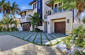 A modern two-story house with a garage, a driveway with patterned paving, and palm trees. - *New* Canal front home with paddle boards, kayaks! (Anna Maria)