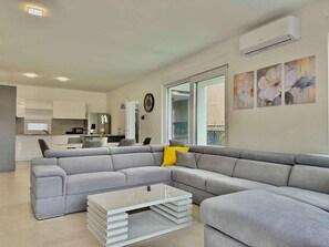 A modern living room with a grey sectional sofa, a white coffee table, and a kitchen in the background. - Villa with swimming pool (Malinska)