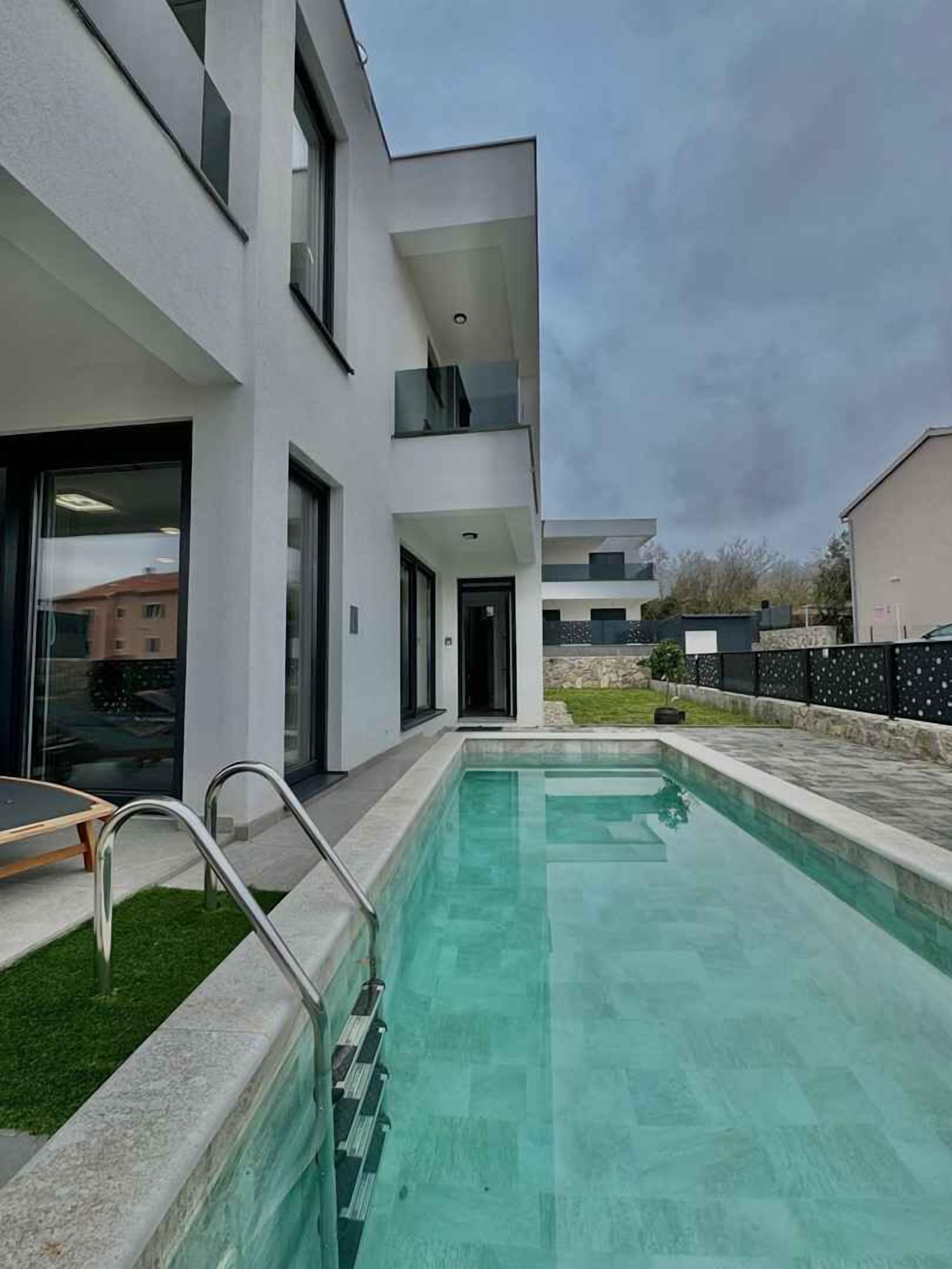 A modern building with a swimming pool, a covered outdoor area, and a visible door.