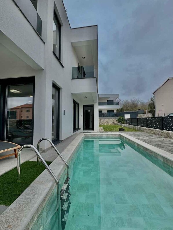 Um edifício moderno com piscina, área externa coberta e uma porta visível.