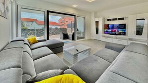 A modern living room with a large flat-screen TV, grey sofas, and a glass sliding door leading to an outdoor area. - Villa with swimming pool (Malinska)