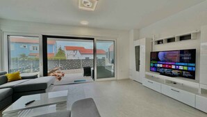 A modern living room with a large flat-screen TV, a sofa, a coffee table, and a sliding glass door leading to a balcony. - Villa with swimming pool (Malinska)