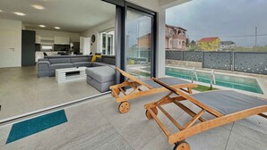 A modern living room with a sectional sofa, a dining area, and a view of a swimming pool. - Villa with swimming pool (Malinska)
