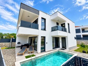 A modern two-story house with a swimming pool, outdoor seating, and a stone wall. - Villa with swimming pool (Malinska)