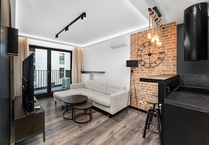 A modern living room with a sectional sofa, a round coffee table, a TV, and a brick accent wall. - Dominikanów Design Loft Apartment (Kraków)