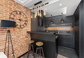 A modern kitchen with a brick wall, a black countertop, and two stools. - Dominikanów Design Loft Apartment (Kraków)
