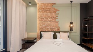 Ein Hotelzimmer mit einem großen Bett, einer Wand aus Ziegelsteinen, einem Nachttisch, einer Lampe und einem Fenster mit Vorhängen.