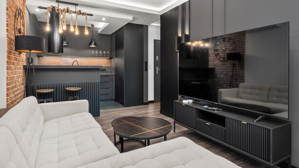 Ein modernes Wohnzimmer mit Sofa, Couchtisch, Fernseher und einer Küchenzeile im Hintergrund.