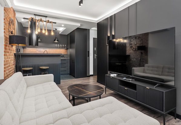 A modern living room with a sofa, a coffee table, a TV, and a kitchen area in the background. - Dominikanów Design Loft Apartment (Kraków)