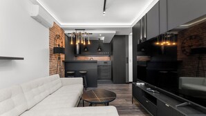 Ein modernes Wohnzimmer mit einer Couch, einem Couchtisch, einem Fernseher und einer Küchenzeile im Hintergrund.