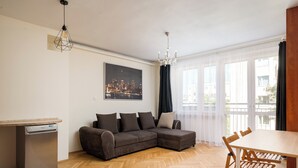 Ein modernes Wohnzimmer mit Fischgrätparkett, einem Ecksofa, einem Esstisch mit Stühlen und einem Geschirrspüler.