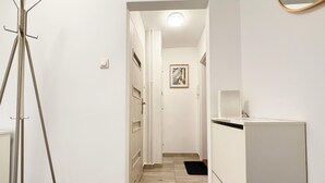 Un couloir avec un trépied, un réfrigérateur blanc et une porte donnant sur une autre pièce.