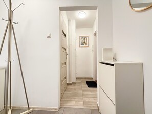 A hallway with a tripod stand, a white refrigerator, and a door leading to another room. - Reja Beige Apartment (Wrocław)