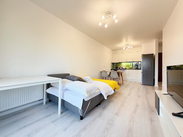A modern, compact living space with a bed, a desk, a kitchen area, and a refrigerator.