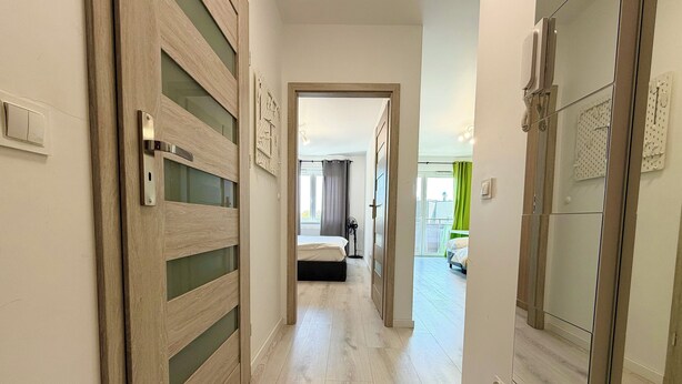 A hotel hallway with wooden doors, a bed in the background, and a view of the outside.