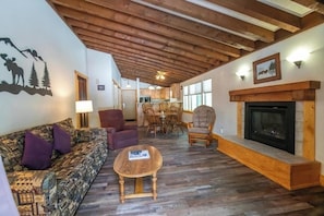 A cozy living room with a fireplace, wooden beams, a sofa, and a dining area.