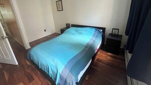 Ein Schlafzimmer mit einem Bett, einem Nachttisch, einer Wanduhr und einer Tür zu einem anderen Raum.