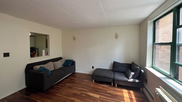 Ein modernes Wohnzimmer mit Holzböden, zwei dunklen Sofas, einem kleinen Tisch und einem großen Fenster.
