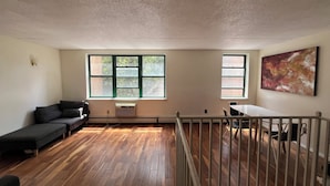 Ein Zimmer mit Holzboden, einer Couch, einem Esstisch, einem Stuhl, einer Geländer und einem Fenster mit Blick auf Bäume.