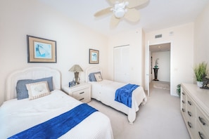 A bedroom with two beds, a ceiling fan, framed artwork, a nightstand, a dresser, and a door leading to another room. - WHITE SANDS BEACHFRONT SUNSET SUNRISE LUX EVERY ROOM SEA POOLS SPAS IN/OUT (Clearwater)