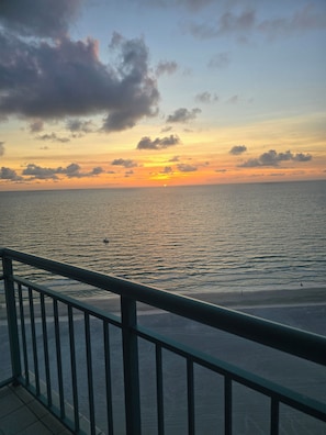 Un coucher de soleil sur une mer calme, avec une rambarde métallique au premier plan.