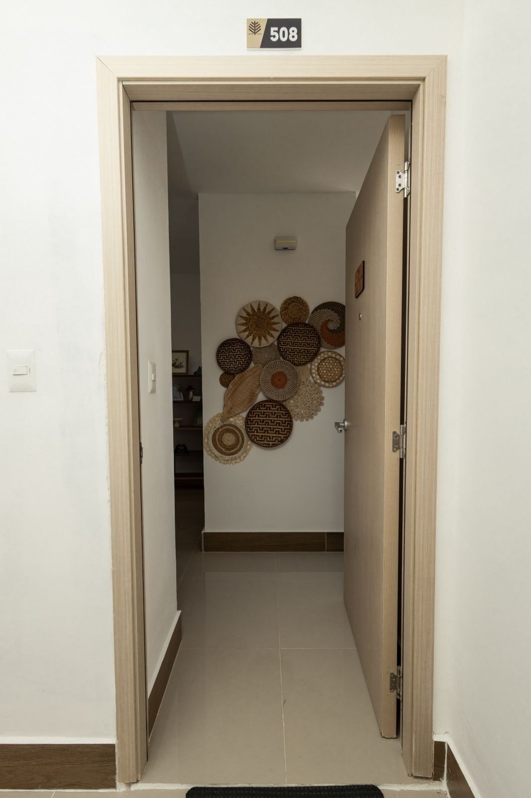 Un pasillo con una puerta marcada '508' que da a una habitación con un muro decorado con diseños circulares tejidos.
