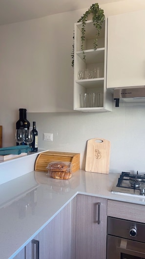 Eine Küche mit einem Gaskochfeld, einem Holzschneidebrett, einer Brotkiste und einer Weinflasche.