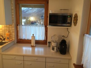 A kitchen with a microwave, coffee maker, and a window with a view of a snowy landscape. - Chesa Chastelets by Interhome (Sils Maria)