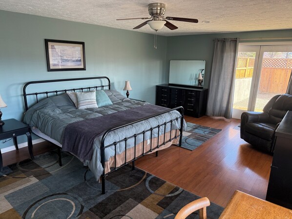 A bedroom with a bed, a desk, a chair, a ceiling fan, a dresser, and a window.