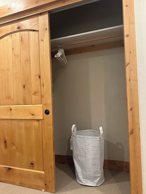 Ein Holzschrank mit Kleiderstange und einem gestreiften Wäschekorb.