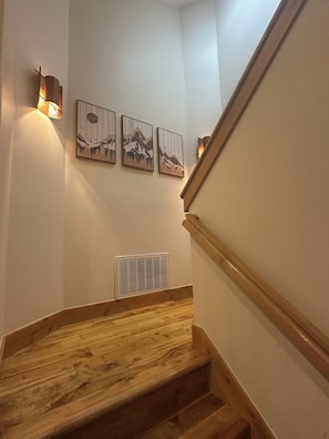 Eine Holztreppe mit Handlauf, einem Wandlüfter und drei gerahmten Kunstwerken.