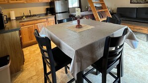 A loft-style living space with a dining area, kitchen, and a wooden staircase. - Peaceful 1-bedroom cabin in charming Talkeetna perfect for getaway (Talkeetna)