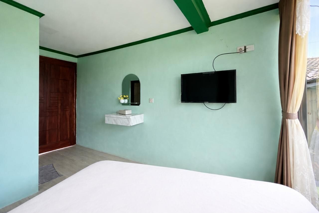 A bedroom with a bed, a TV mounted on the wall, a small shelf with a mirror, and a wooden door.