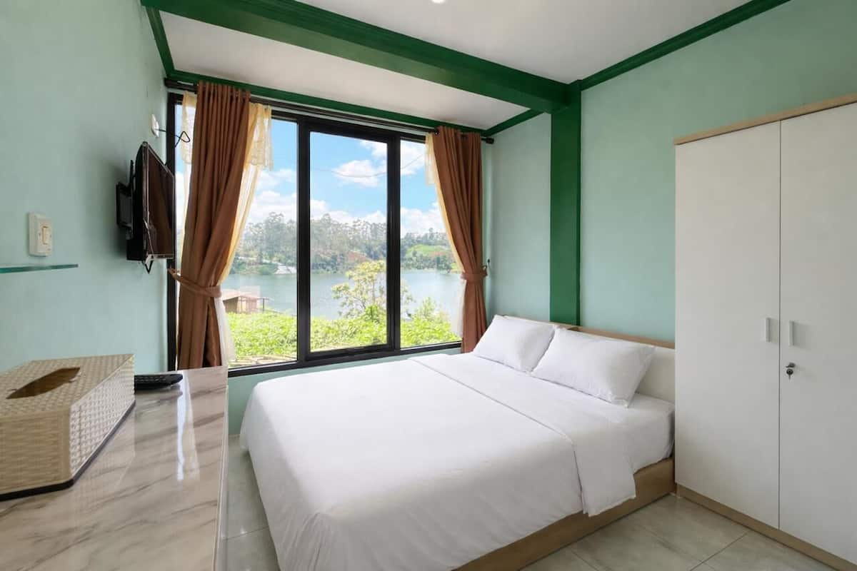 Une chambre à coucher avec un lit, une armoire, une télévision et une fenêtre avec des rideaux.
