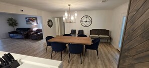 Un comedor con una mesa de madera, seis sillas, una araña, un reloj y un sofá.