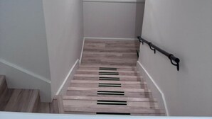 En trappa med trästeg, en tavla föreställande en blå fågel som hänger på väggen, och två väggmonterade lampor.